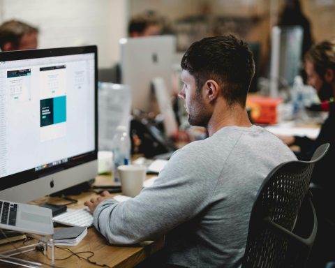 man in gray sweatshirt sitting on chair in front of iMac