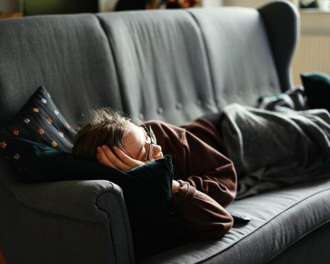 woman in pink jacket lying on gray couch