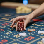 A hand holding poker chips on a roulette table, showcasing gambling and casino gaming.