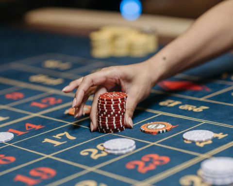 A hand holding poker chips on a roulette table, showcasing gambling and casino gaming.