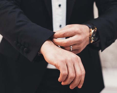 A man's hands adjusting the cuffs of his black suit