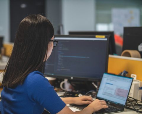 woman using black laptop computer near turned on flat screen computer monitor