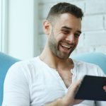 Man laughing while holding credit card and tablet.