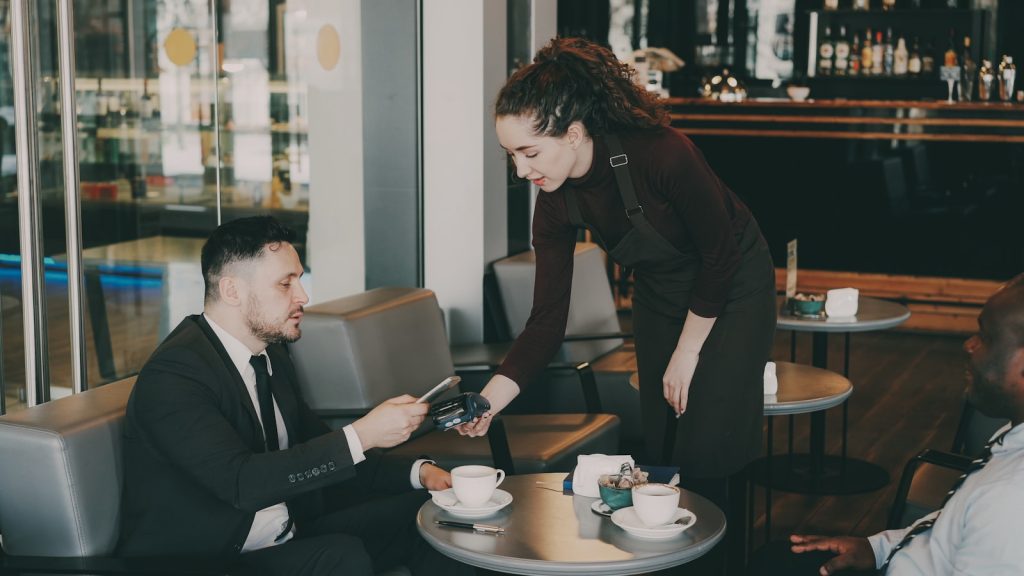 A woman serves coffee to a man in a cafe.