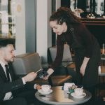 A woman serves coffee to a man in a cafe.