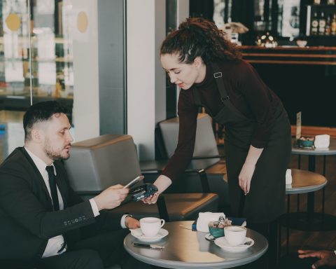 A woman serves coffee to a man in a cafe.