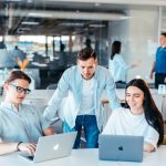 a group of people sitting around a table with laptops