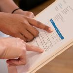 Two people pointing at financial details on a document, highlighting invoice analysis.