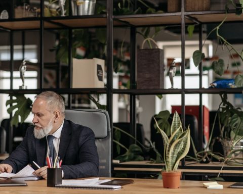 A senior man in a suit working at a desk in a modern office with plants.