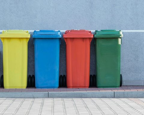 four assorted-color trash bins beside gray wall