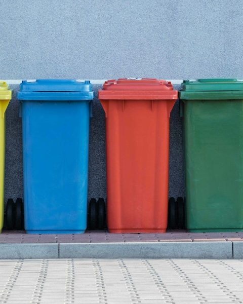 four assorted-color trash bins beside gray wall