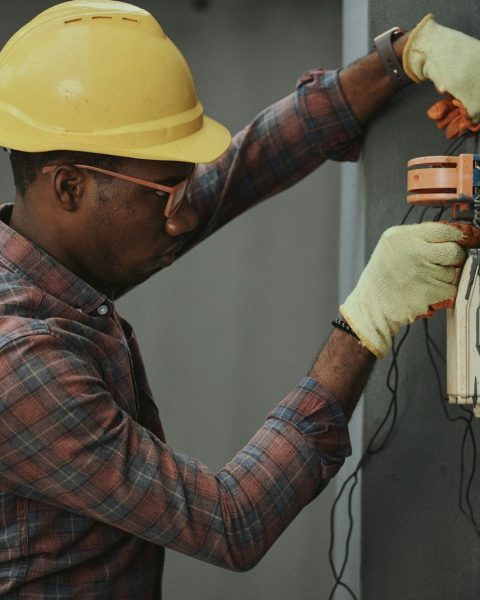 man in brown and white plaid dress shirt and yellow hard hat holding black and orange