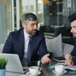 a couple of men sitting at a table in front of a laptop
