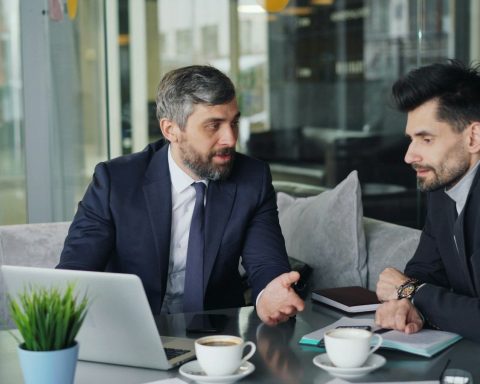 a couple of men sitting at a table in front of a laptop