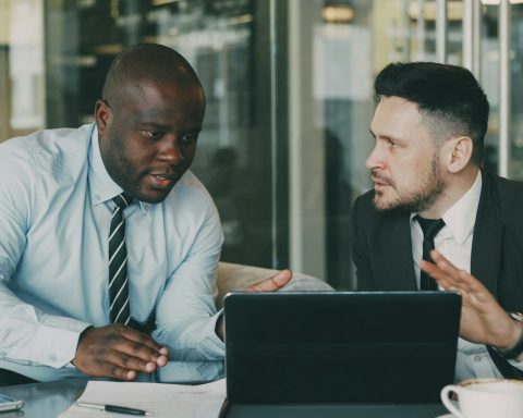 Two businessmen collaborating over a tablet and laptop