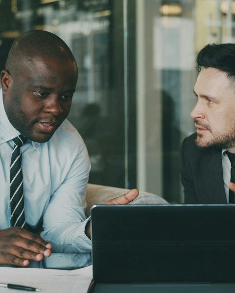Two businessmen collaborating over a tablet and laptop