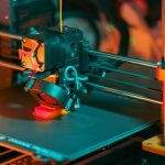 3D printer creating a red object with yellow filament